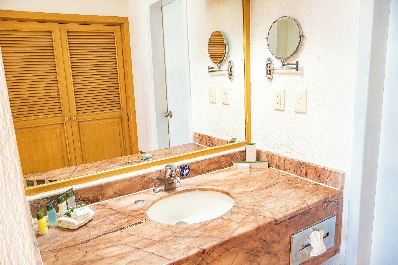 A bathroom with a marble sink, two mirrors, a towel rack, and a wooden door.