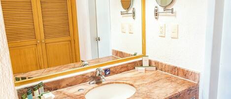 A bathroom with a marble sink, two mirrors, a towel rack, and a wooden door.