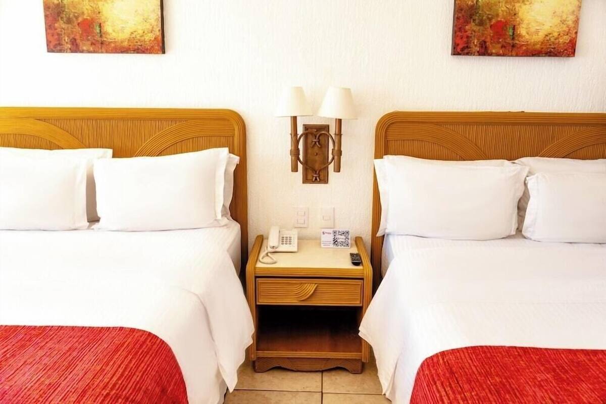 Habitación de hotel con dos camas, una mesita de noche con lámpara, teléfono y un código QR.