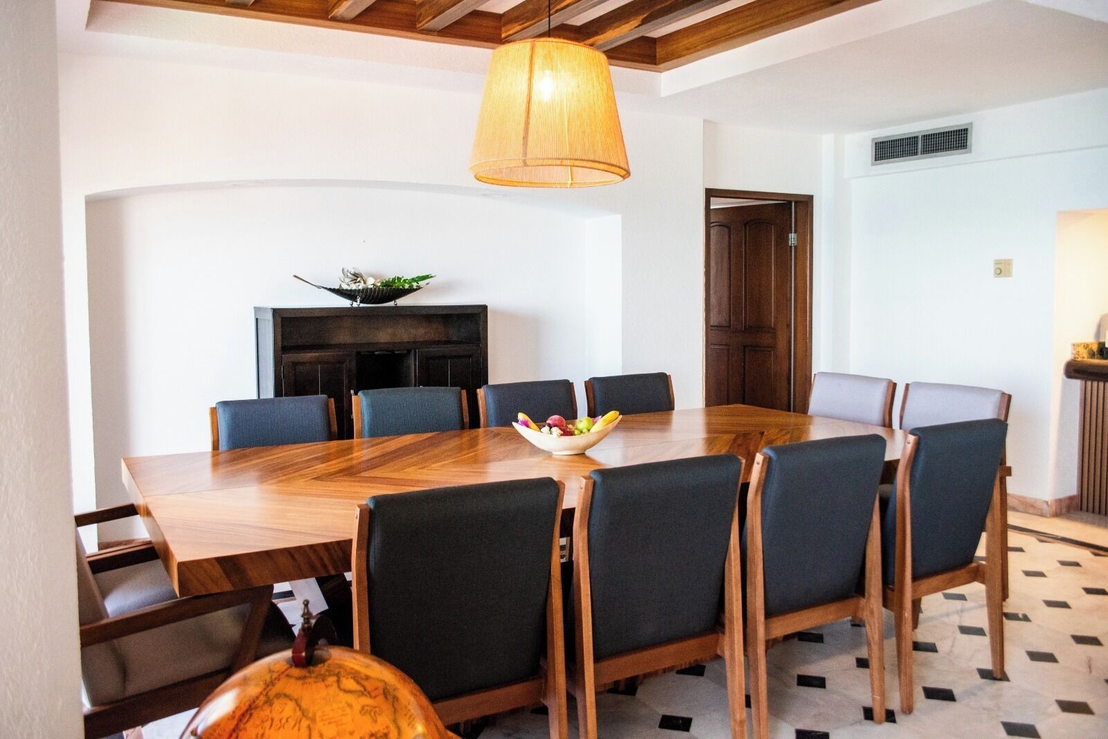 Un comedor con una mesa de madera, seis sillas, un globo terráqueo y un frutero.