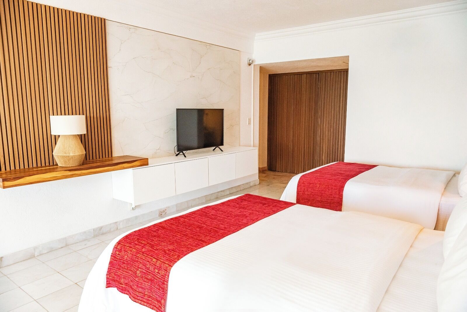 Habitación de hotel con dos camas, televisión, panel de pared de madera y una manta roja.