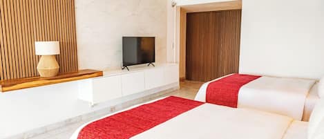 A hotel room with two beds, a TV, a wooden panel wall, and a red throw blanket.