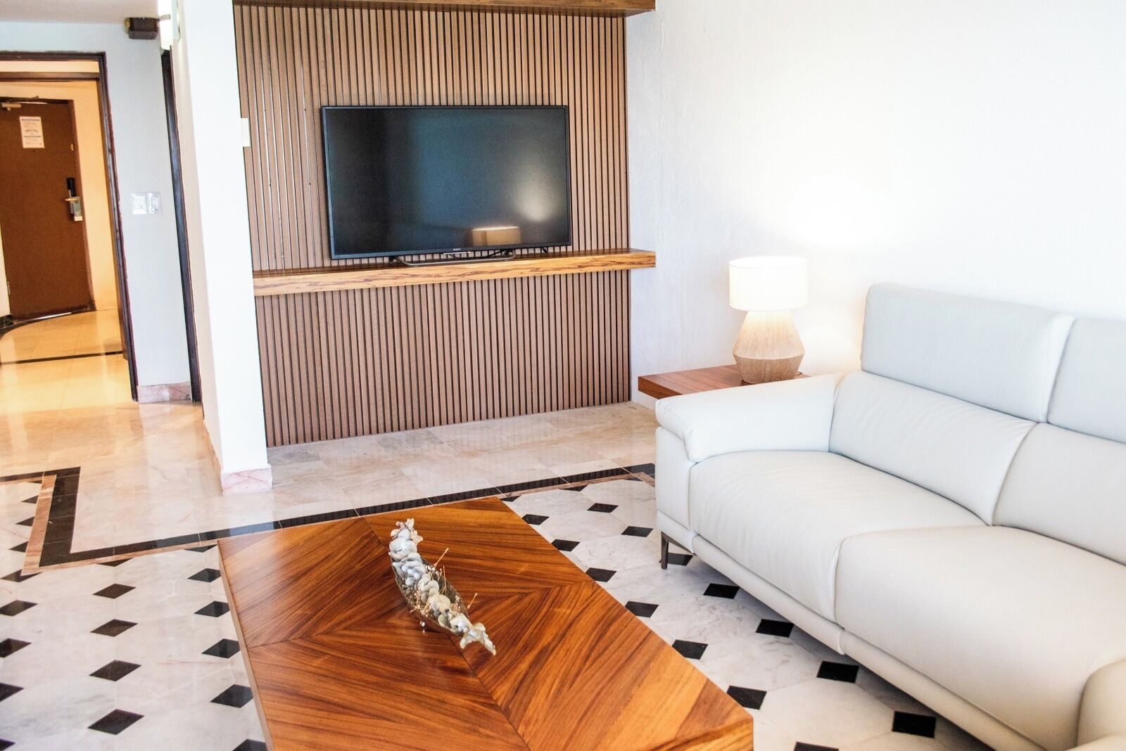 Un soggiorno moderno con una TV a schermo piatto montata su una parete in legno, un divano bianco, un tavolino in legno e un pavimento decorato.