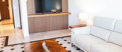 Un soggiorno moderno con una TV a schermo piatto montata su una parete in legno, un divano bianco, un tavolino in legno e un pavimento decorato.