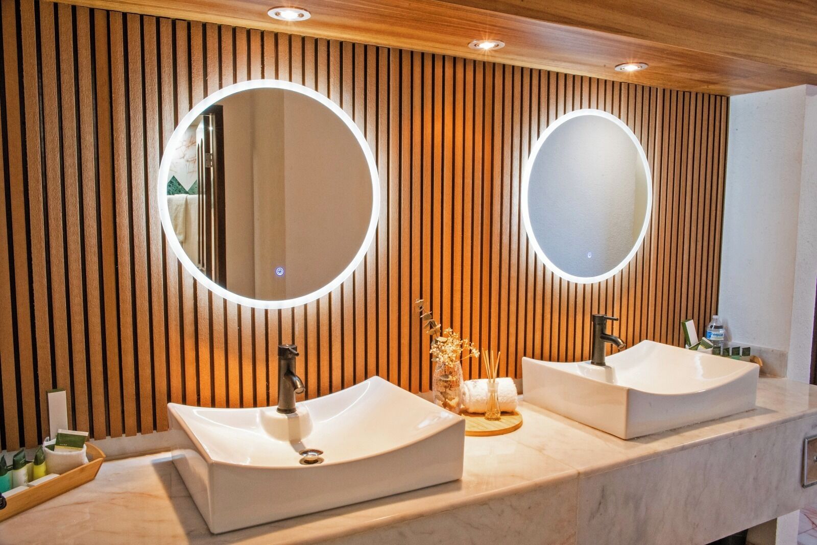 Une salle de bain moderne avec deux lavabos, un lambris en bois et des miroirs ronds.