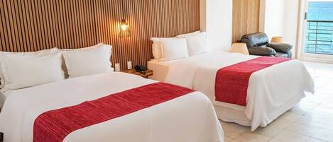 A hotel room with two beds, a wooden slat headboard, a nightstand, a lamp, and a view of the sea.