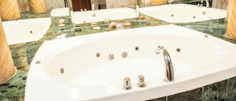 A large, oval-shaped bathtub with a single faucet, surrounded by a marble countertop.