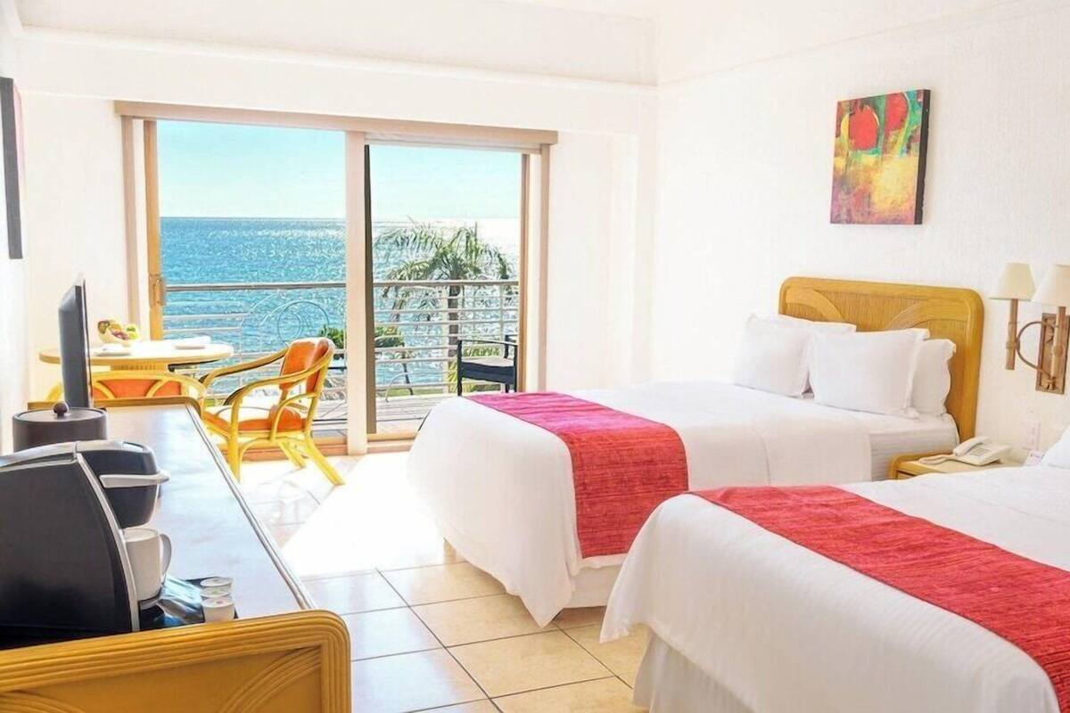 Habitación de hotel con dos camas, un escritorio con ordenador, una silla y vista al océano.