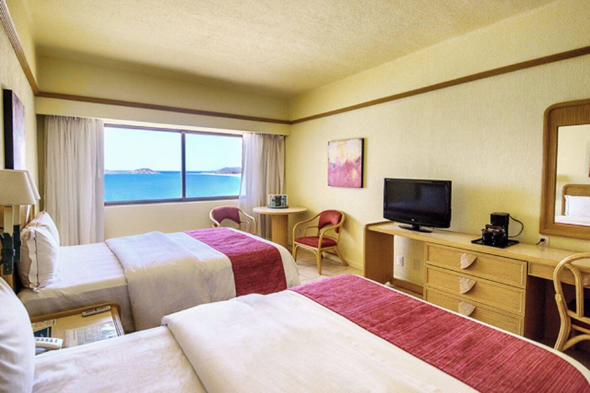 Una habitación de hotel con dos camas, televisión, escritorio y una silla.
