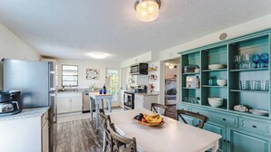 Eine Küche mit Esstisch, Stühlen, einem Kühlschrank, einer Mikrowelle und einem türkisblauen Schrank mit Geschirr.