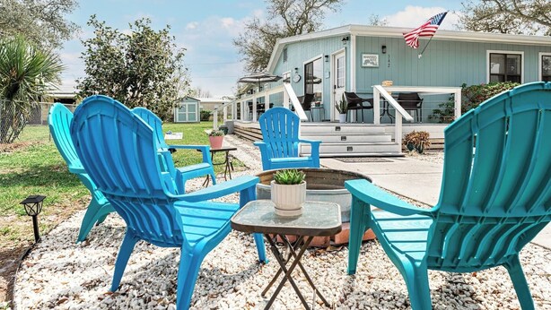 Eine Terrasse mit türkisfarbenen Adirondack-Stühlen, einem kleinen runden Tisch und einem Topfpflanzen.
