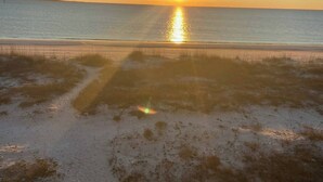 Ein Strand mit freiem Blick auf den Ozean und einer untergehenden Sonne in der Ferne.