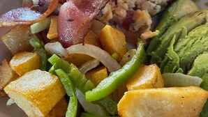 A plate of food with bacon, scrambled eggs, avocado, roasted potatoes, and green peppers.