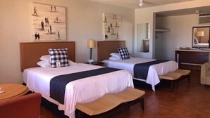 A hotel room with two beds, a desk, a chair, and artwork on the walls.