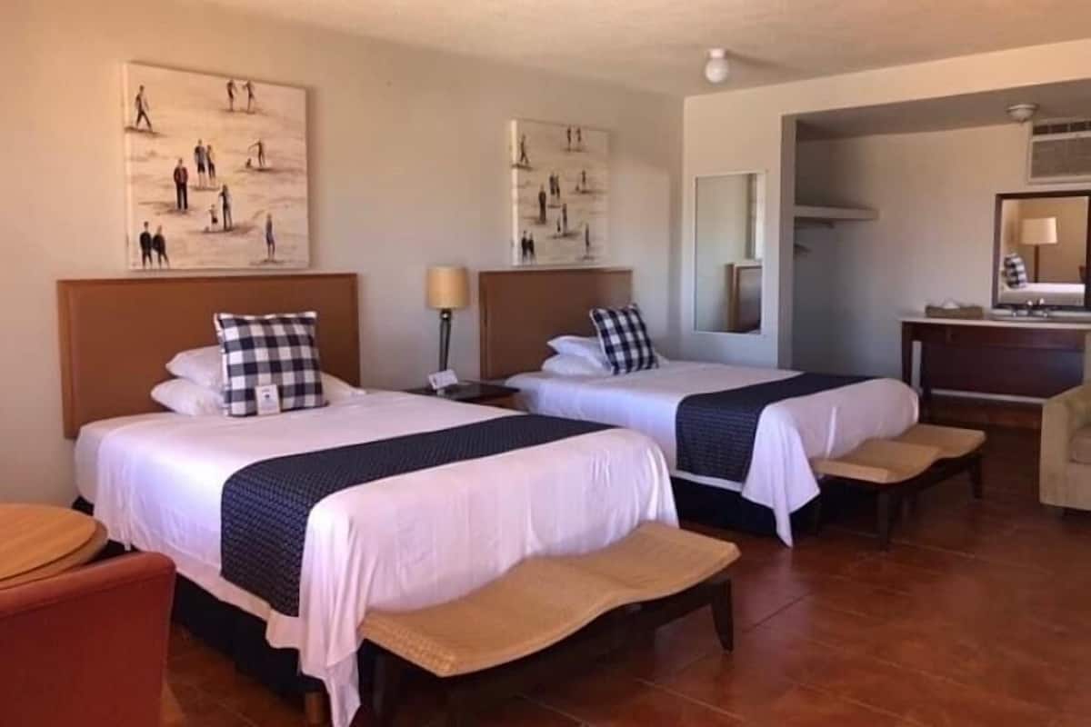 A hotel room with two beds, a desk, a chair, and artwork on the walls.