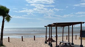 A beach with a wooden gazebo, picnic tables, and a palm tree.