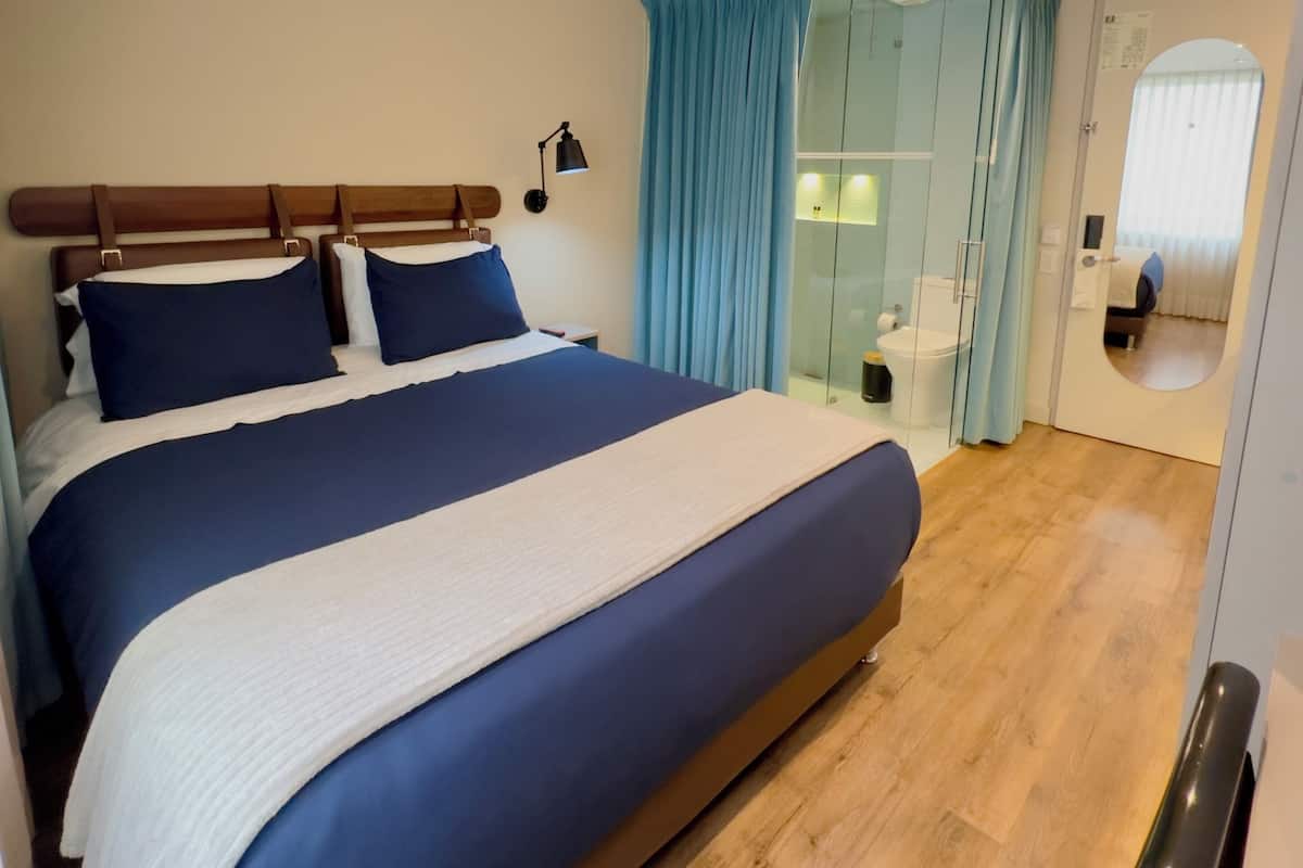 Una habitación de hotel moderna con una cama grande, un baño con cabina de ducha de vidrio y un espejo en la pared.