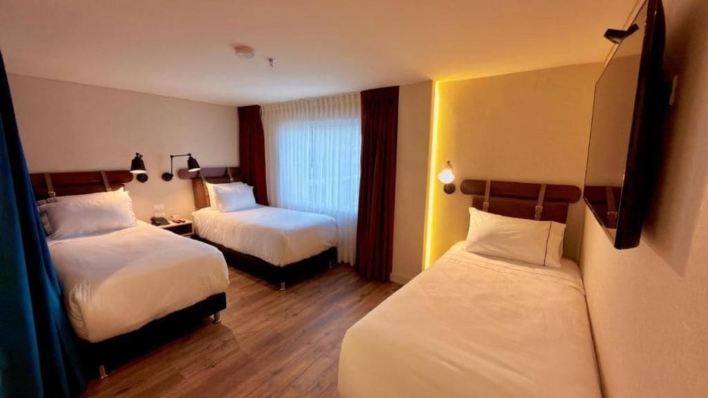 A hotel room with two beds, a wooden floor, and a large mirror on one wall.