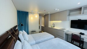 Una habitación de hotel con dos camas, un escritorio con televisor, una kitchenette pequeña y un baño.