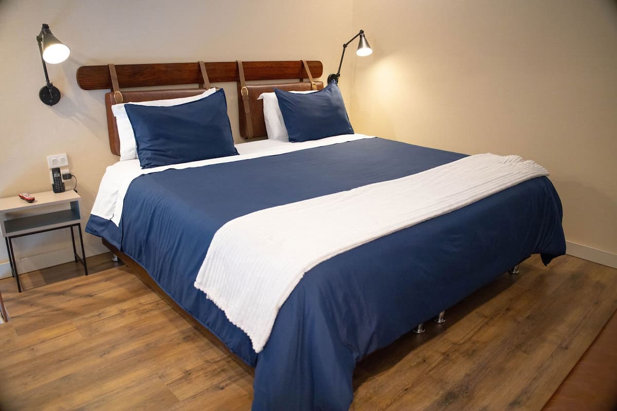 Una cama bien hecha, con cabecera, mesitas de noche y lámparas de pared.