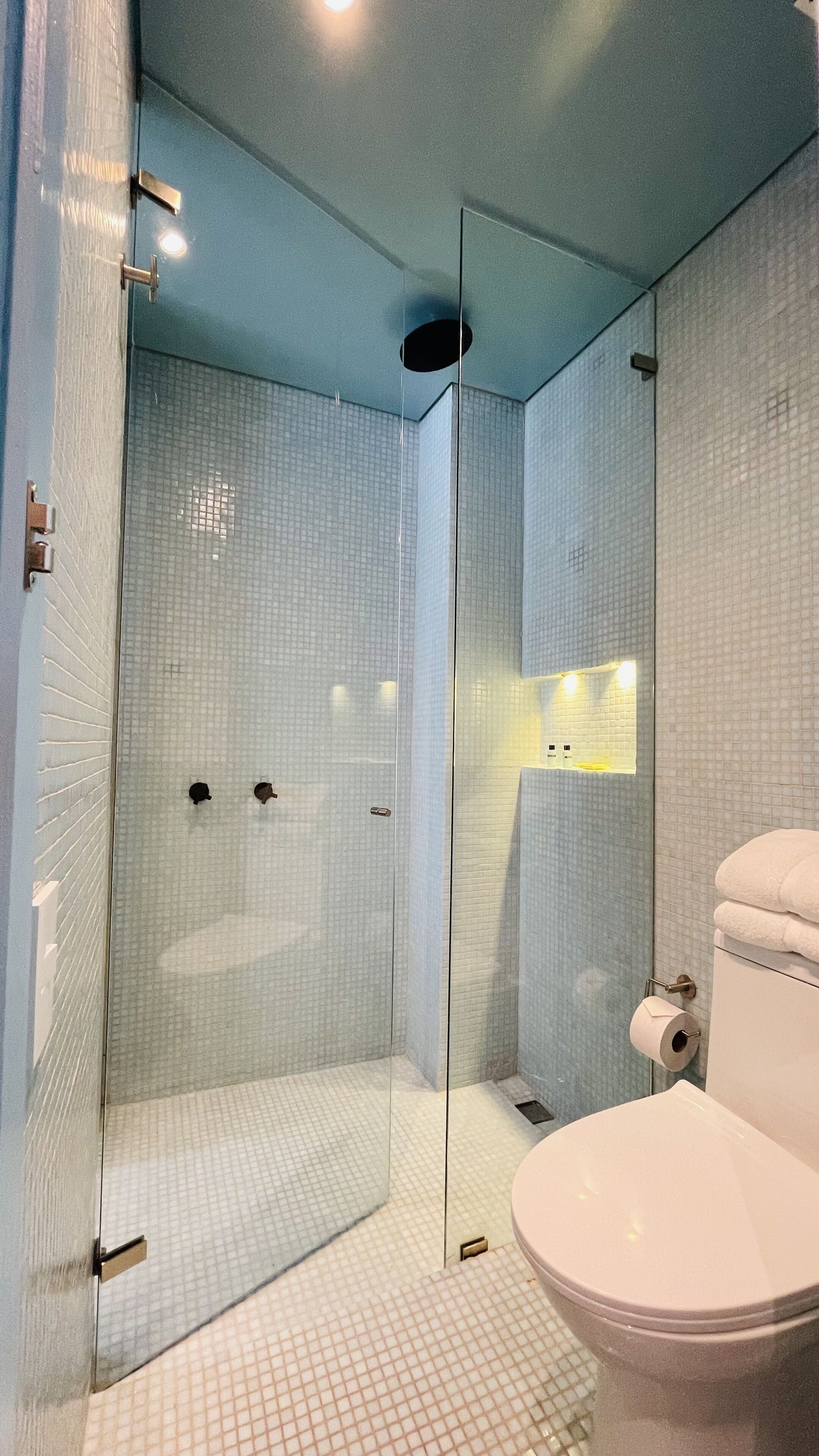 Une salle de bain moderne avec une douche à parois de verre, des toilettes blanches et un petit coin lavabo.