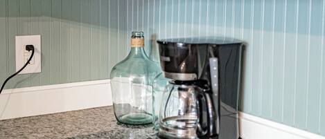 Una cocina con armarios blancos, una cafetera y una botella de vidrio sobre una encimera de granito.