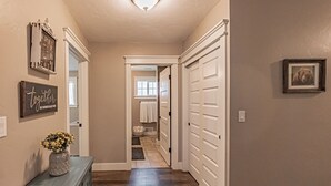 Un pasillo con piso de madera, un aparador con un florero y una puerta que da al baño.