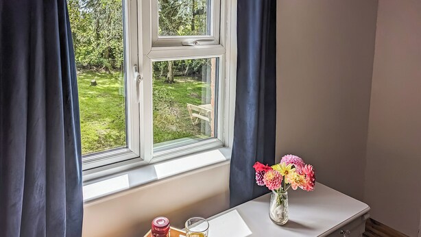 A window with a view of a garden, a tray with croissants, a glass of orange juice, and a vase with flowers on a white dresser. - A nature lovers delight. (Ludham)