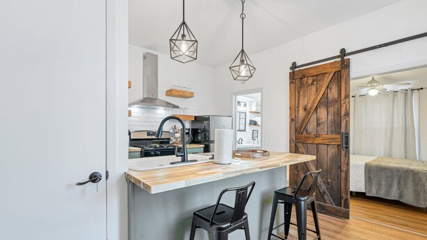 Een compacte keuken met een houten aanrecht, twee hangende吊灯en een schuifdeur in boerderijstijl die naar een slaapkamer leidt.