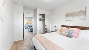 Een slaapkamer met een bed, een nachtkastje, een kunstwerk aan de muur en wanddecoratie van macramé.