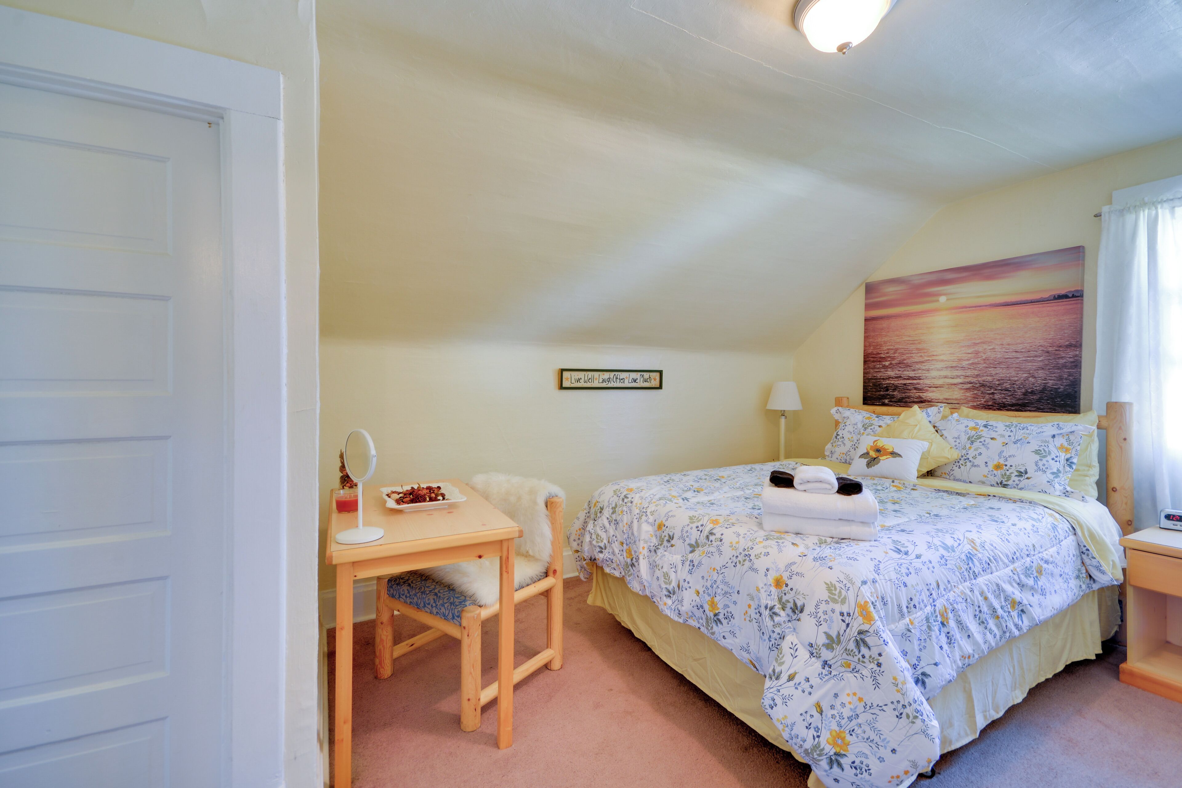 A bedroom with a bed, a desk, a chair, a nightstand, and a painting on the wall.