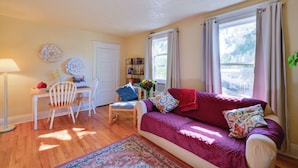 A cozy living room with a sofa, a dining table with chairs, a lamp, and a bookshelf.