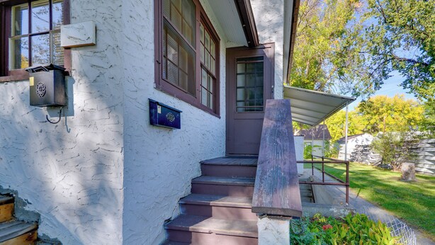 A white building with a wooden staircase leading to a door, a mailbox, and a garden area with a fence.