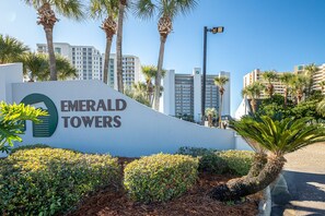 A sign for Emerald Towers with a modern design, surrounded by well-maintained landscaping and palm trees.