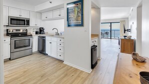 A modern kitchen with white cabinets, stainless steel appliances, and a wooden dining table. - Spectacular Ocean/Beach Front Condo, Awesome view of Gulf- w/ Free Beach Service (Destin)