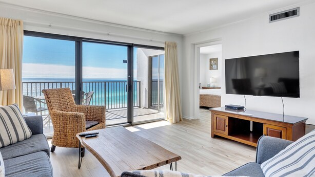A modern living room with a large TV, comfortable seating, a wooden coffee table, and a balcony with a view of the ocean. - Spectacular Ocean/Beach Front Condo, Awesome view of Gulf- w/ Free Beach Service (Destin)