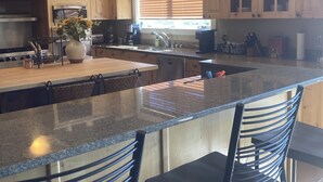 Eine moderne Küche mit Granit-Arbeitsplatten, Edelstahlgeräten, Holzschränken und einer großen Kochinsel mit Barhocker.