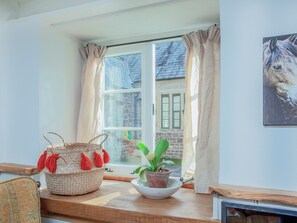Une pièce avec une fenêtre, un panier en osier, une plante en pot et un tableau encadré au mur.