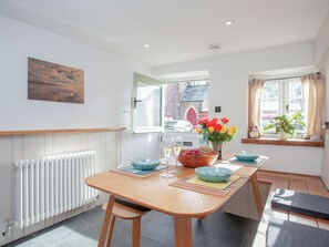 A dining area with a table, chairs, a radiator, a window with curtains, and a view of a building outside.
