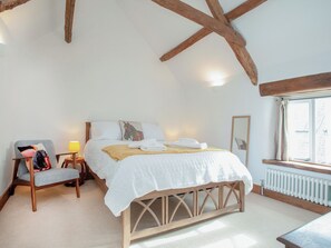 Une chambre à coucher avec un lit, une chaise, une lampe, une fenêtre et des poutres en bois au plafond.