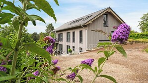 Een houten gebouw met een schuin dak, een grindpad en paarse bloemen op de voorgrond.