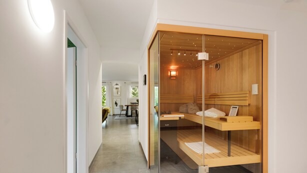 Een moderne hotelkamer met een glazen scheidingswand, een houten bankje en een kleine tafel.