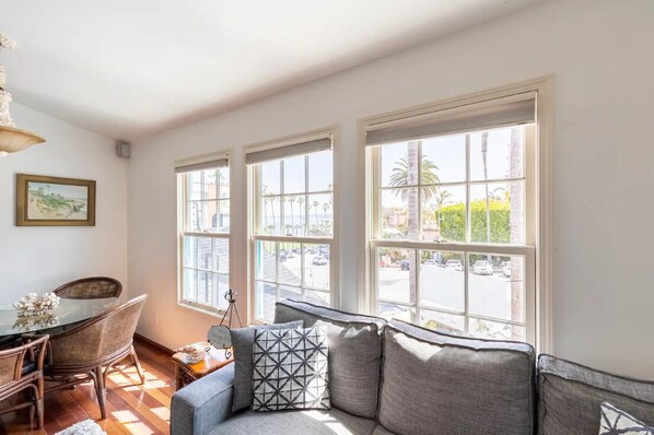 A living room with a sofa, a dining table with chairs, and large windows with a view of the street. - Steps to La Jolla Cove with Gorgeous Views, Village Living at its Finest! (San Diego)