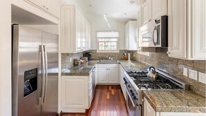 A modern kitchen with white cabinetry, stainless steel appliances, granite countertops, and a wood floor. - Steps to La Jolla Cove with Gorgeous Views, Village Living at its Finest! (San Diego)