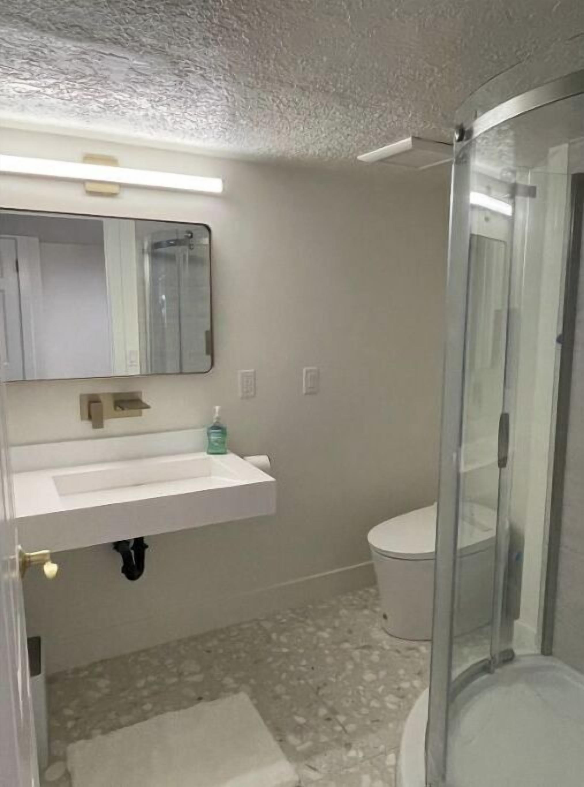 Un baño con lavamanos blanco, un espejo, inodoro y cabina de ducha de vidrio.