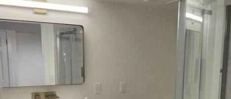 Un baño con lavamanos blanco, un espejo, inodoro y cabina de ducha de vidrio.