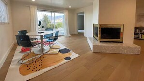 Een moderne woonkamer met een eethoek, een open haard en een groot raam met uitzicht op het omliggende landschap.