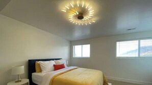 Een slaapkamer met een bed, een nachtkastje met een lamp en een plafondlamp.