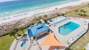 Vista aérea de un complejo turístico frente a la playa con piscina, sombrillas y una torre de salvavidas.