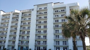 Un hotel de varios pisos con balcones, mobiliario exterior y una palmera.